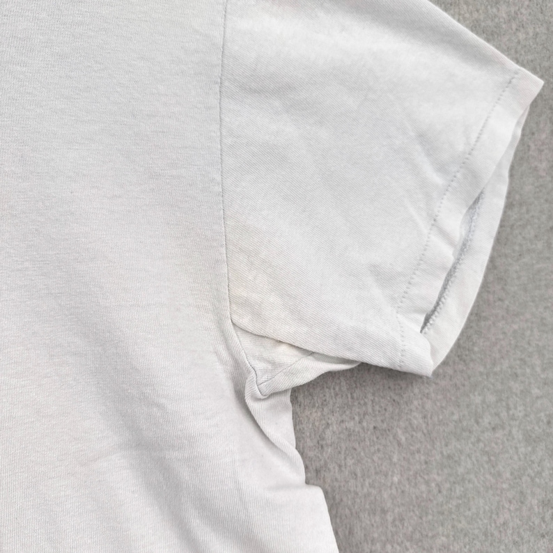May include: Close-up of a light gray t-shirt sleeve. The sleeve is short and has a stitched hem. The fabric appears to be a soft, lightweight material. The shirt is plain and without any visible graphics or patterns.