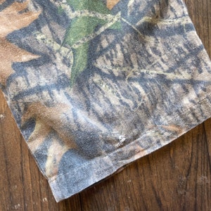 May include: Close-up of a brown, green, and gray camouflage fabric with a stitched seam. The fabric has a textured, slightly worn appearance.