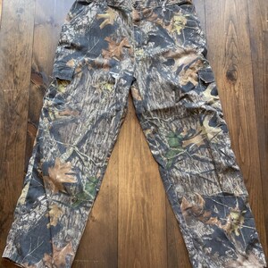 May include: Camouflage cargo pants with a brown, green, and black pattern. The pants have two large pockets on the sides.