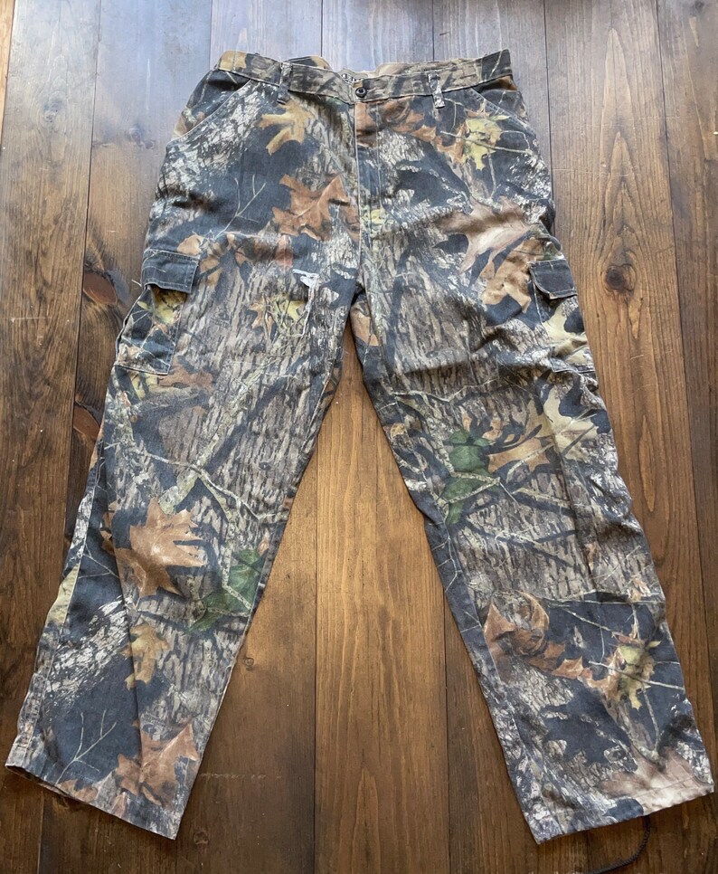 May include: Camouflage cargo pants with a brown, green, and black pattern. The pants have two large pockets on the sides.