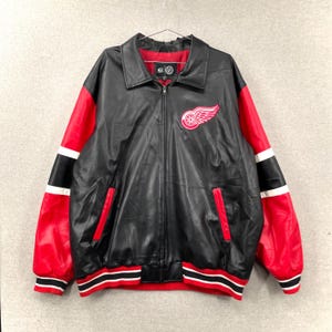 May include: Black and red leather jacket with a zip-up front. The jacket has red sleeves with black and white stripes, a collar, and a logo on the chest. The jacket has a ribbed hem and cuffs with red and white stripes.