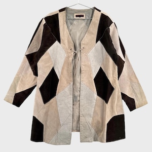 May include: A long-sleeve jacket featuring a geometric patchwork design in shades of dark brown, tan, and cream. The jacket has a V-neckline, an open front with a thin tie closure, and a smooth interior lining. The exterior is made of suede.