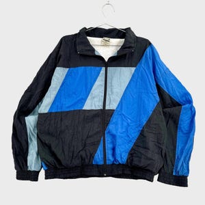 Peut inclure: Une veste zippée à manches longues présentant un design color-block en noir, bleu roi et bleu clair. La veste possède un col montant, une fermeture éclair intégrale, des poignets élastiques et un ourlet élastique, avec une doublure blanche.
