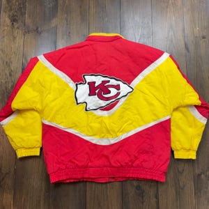 May include: A vintage Kansas City Chiefs jacket in red and yellow with a white and red team logo on the back. The jacket has a zip fastening and a white stripe down each sleeve.