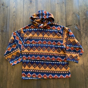 May include: A patterned fleece hoodie with a Southwestern design. The colours include navy blue, rust, gold, and white geometric shapes. It has a kangaroo pocket and a drawstring hood.