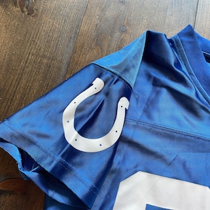 May include: Blue football jersey with a white horseshoe logo on the shoulder. The jersey has a white number on the front.