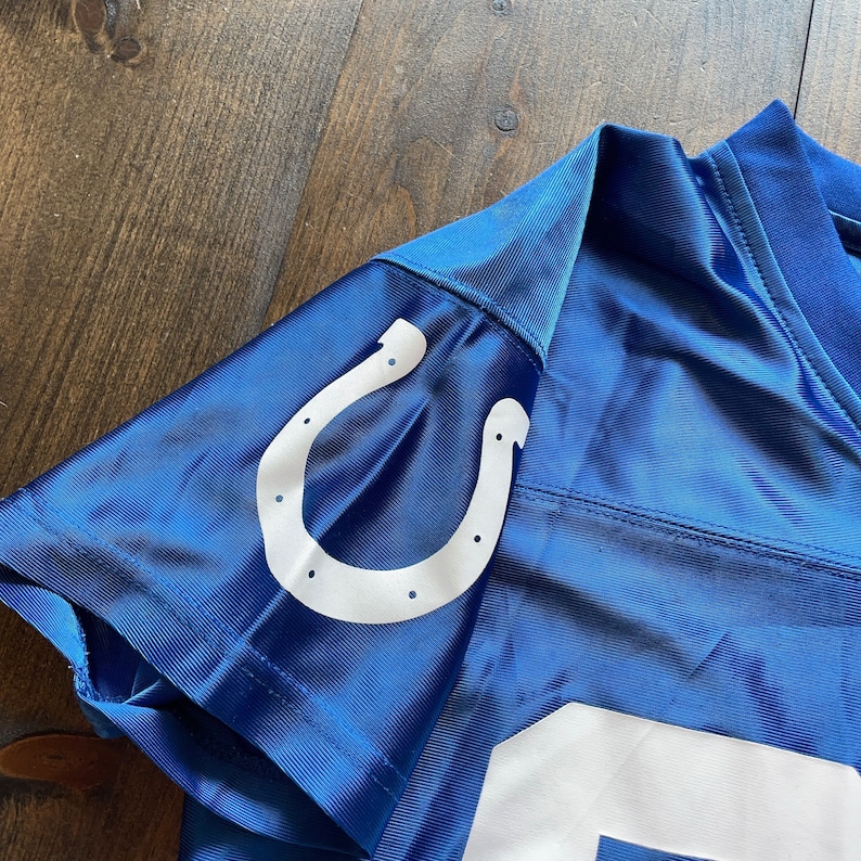May include: Blue football jersey with a white horseshoe logo on the shoulder. The jersey has a white number on the front.
