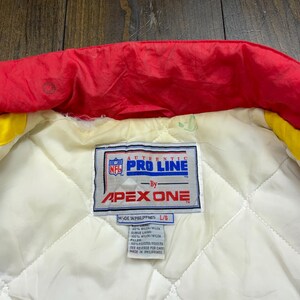 May include: A white label with the text "AUTHENTIC NFL PRO LINE -By- APEX ONE" and "MADE IN PHILIPPINES L/B 100% NYLON/NYLON SLEEVE LINING 100% NYLON/NYLON FILLER: SEE REVERSE FOR CARE MADE IN PHILIPPINES".