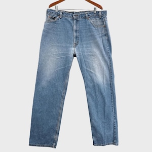 May include: A pair of light blue denim jeans featuring a classic five-pocket design, a button fly closure, and a straight-leg cut. The fabric displays a faded wash pattern across the front thighs and hips, with visible copper-toned rivets.