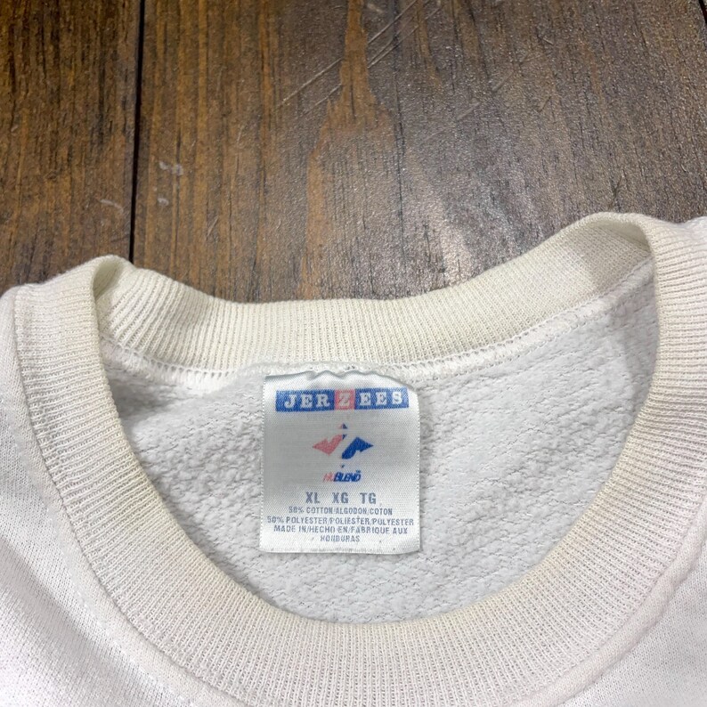 May include: White sweatshirt with a Jerzees tag. The tag says "XL XG TG" and lists the fabric content as 50% cotton and 50% polyester. The tag also says "Made in Honduras".