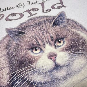 May include: A white t-shirt with a gray cat illustration and the text "As a matter of fact, the world revolves around me."