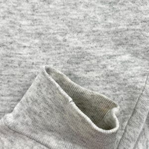May include: Close-up of a grey sweatshirt sleeve cuff. The cuff is folded over, revealing the inside fabric. The material is a heathered grey, with a ribbed texture on the cuff and a smoother texture on the body of the sleeve.