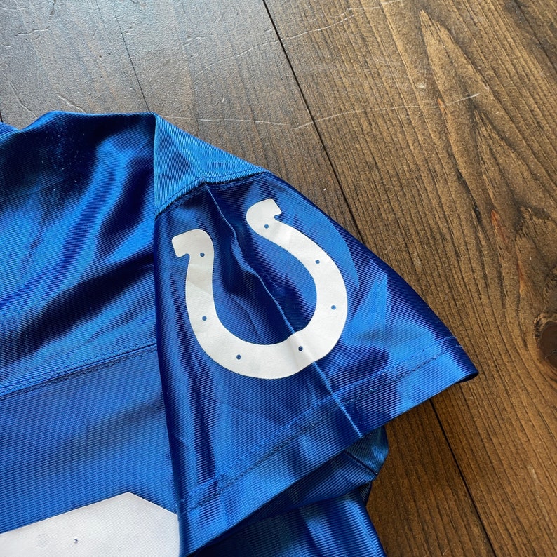 May include: Blue football jersey with a white horseshoe logo on the sleeve.