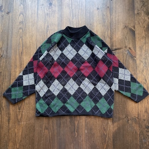 May include: A black sweater with a diamond pattern in shades of green, red, and white.