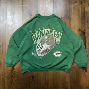 May include: Green and yellow vintage Green Bay Packers sweatshirt with a cartoon football helmet graphic and the text "Green Bay Packers".
