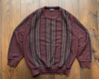 May include: A maroon sweater with a striped pattern in shades of brown, black, and white. The sweater has a crew neck and long sleeves.