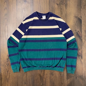 May include: A vintage crew neck sweatshirt with horizontal stripes in navy blue, teal, and cream. The long-sleeved top is made of a soft material and has a classic, casual style. The sweatshirt is laid flat on a wooden surface.