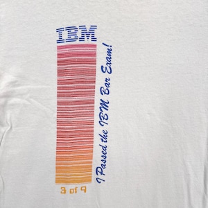 May include: White t-shirt with the IBM logo in blue and a vertical striped design in red, orange, and yellow. The text "I Passed the IBM Bar Exam!" is in blue, and "3 of 9" is at the bottom.