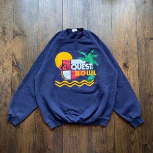 Peut inclure: Un sweat-shirt bleu marine avec un motif représentant un palmier, un soleil et le texte "CARQUEST BOWL GEORGIA TECH" en lettres colorées.