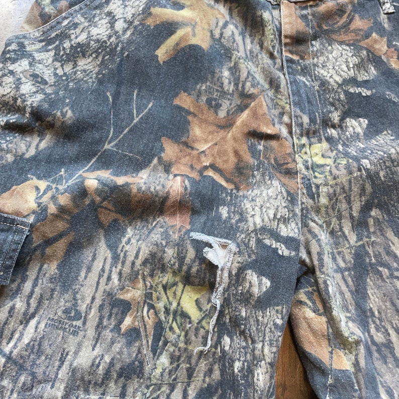 May include: Camouflage print pants with a small tear in the fabric. The pants are made of a soft, comfortable material and have a relaxed fit.