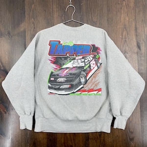 May include: A grey crew neck sweatshirt with a race car graphic. The design features the text "Kelly Tapper" in blue and red, and the number 85 on the car. The word "Mustang" is visible at the bottom of the car.