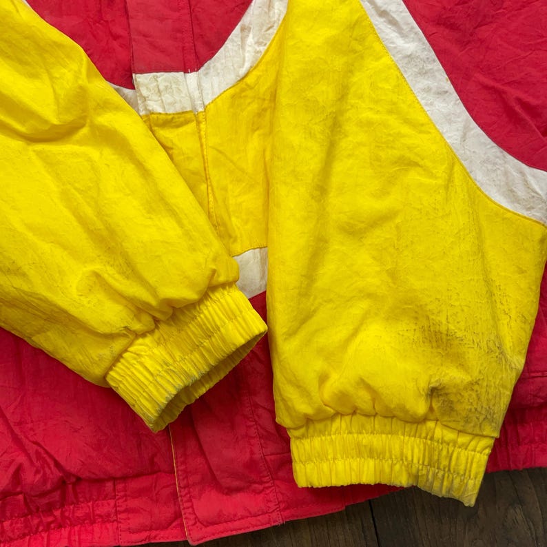 May include: A red and yellow jacket with white stripes. The jacket has a zip fastening and elastic cuffs.