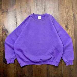 May include: A purple crew neck sweatshirt. The sweatshirt is made of a soft, comfortable material.