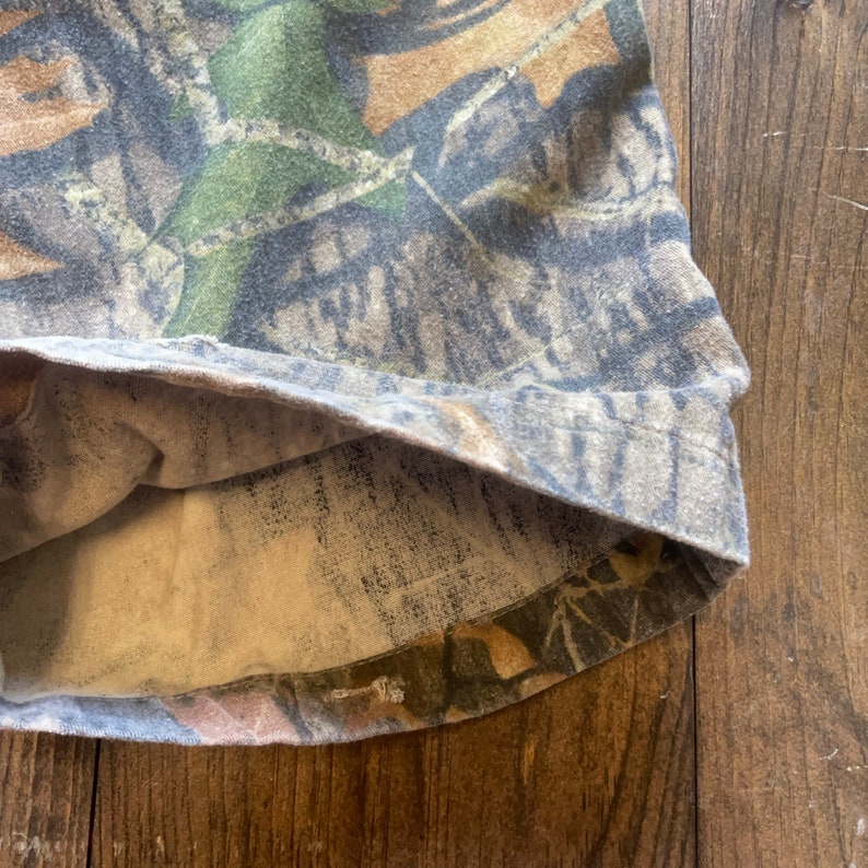May include: Close-up of the inside of a camouflage-patterned shirt. The fabric is a light brown color with a subtle texture.