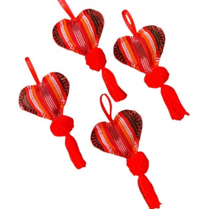 May include: Four heart-shaped ornaments with red, orange, and white striped fabric. Each ornament has a red tassel and a loop of red ribbon for hanging. The ornaments are on a white background.