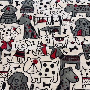 May include: A cream-coloured fabric pattern with a repeating design of cartoon dogs in black, grey, and red. The dogs are in various poses and have different markings, some wearing collars or sweaters. Black bone shapes are scattered throughout the design.