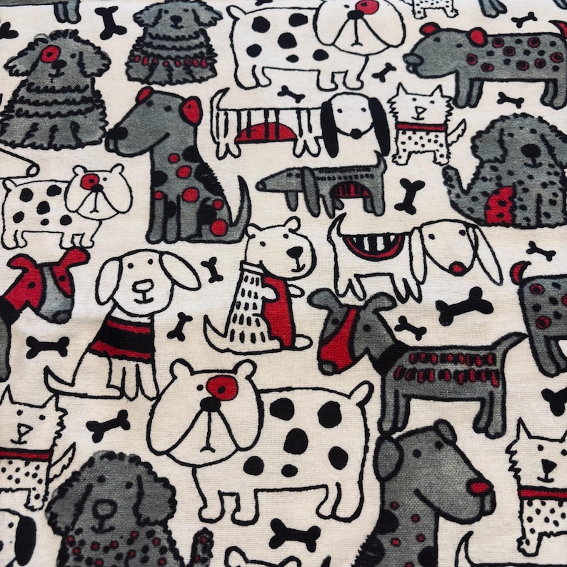May include: A cream-coloured fabric pattern with a repeating design of cartoon dogs in black, grey, and red. The dogs are in various poses and have different markings, some wearing collars or sweaters. Black bone shapes are scattered throughout the design.