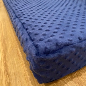 May include: A close-up of a navy blue dog bed with a textured, quilted surface. The bed has a thick, plush border.