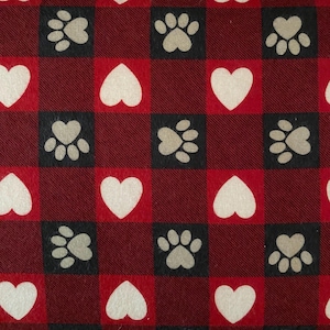 May include: A repeating pattern of red and black squares featuring white hearts and paw prints. The paw prints are in black squares and the hearts are in red squares. The background is a dark red fabric.