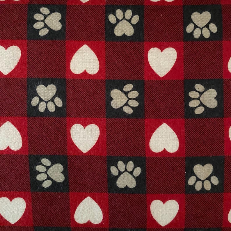 May include: A repeating pattern of red and black squares featuring white hearts and paw prints. The paw prints are in black squares and the hearts are in red squares. The background is a dark red fabric.