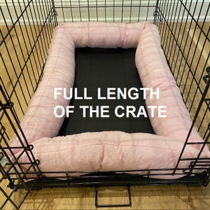 May include: Pink quilted dog bed liner inside a black metal dog crate. The liner is the full length of the crate. "FULL LENGTH OF THE CRATE" is written in white text on the liner.