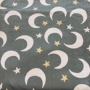 May include: A textile featuring a repeating pattern of white crescent moons and yellow stars on a muted green backdrop. The celestial design is evenly spaced, creating a whimsical and dreamy aesthetic across the fabric.