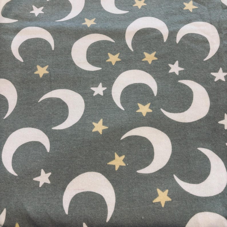 May include: A textile featuring a repeating pattern of white crescent moons and yellow stars on a muted green backdrop. The celestial design is evenly spaced, creating a whimsical and dreamy aesthetic across the fabric.