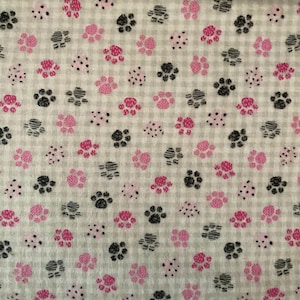 May include: A fabric featuring a repeating pattern of pink and black paw prints and small dots on a light grey checkered background. The paw prints vary in size and direction, creating a playful design.