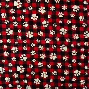 May include: A fabric featuring a red and black check pattern, reminiscent of buffalo plaid. White paw prints are scattered across the fabric. The paw prints vary in size and are evenly distributed.