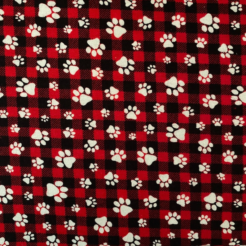 May include: A fabric featuring a red and black check pattern, reminiscent of buffalo plaid. White paw prints are scattered across the fabric. The paw prints vary in size and are evenly distributed.