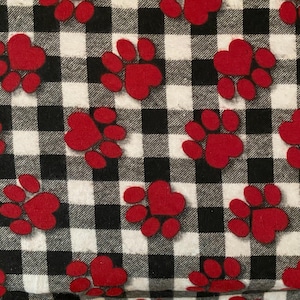 May include: A black and white checked fabric with a repeating pattern of red paw prints. Each paw print has a heart-shaped center. The design is suitable for pet-themed crafts or accessories.