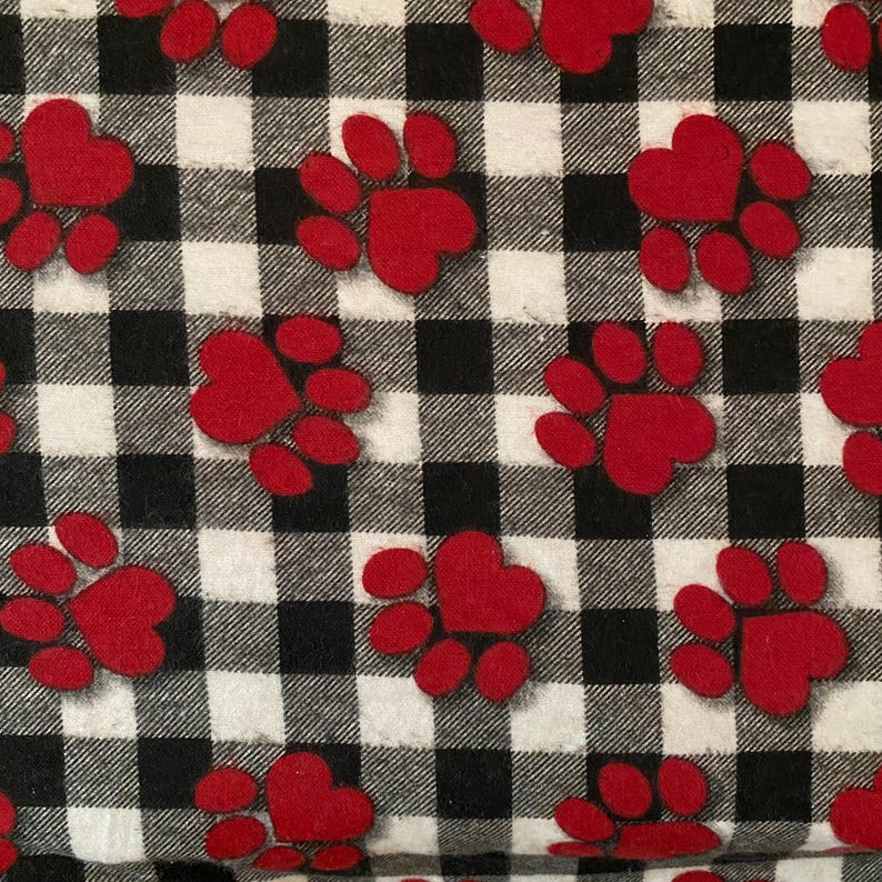 May include: A black and white checked fabric with a repeating pattern of red paw prints. Each paw print has a heart-shaped center. The design is suitable for pet-themed crafts or accessories.