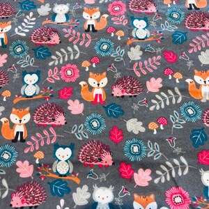 May include: Grey fabric featuring a repeating pattern of cartoon foxes, owls, and hedgehogs. The design includes pink, teal, and white flowers, mushrooms, and leaves. The animals are orange, white, and black.