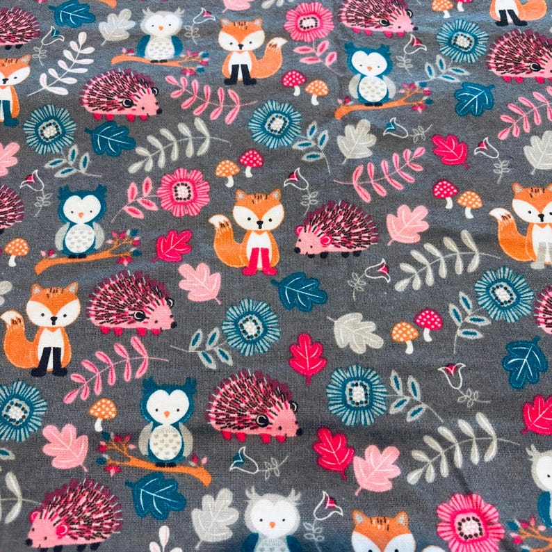 May include: Grey fabric featuring a repeating pattern of cartoon foxes, owls, and hedgehogs. The design includes pink, teal, and white flowers, mushrooms, and leaves. The animals are orange, white, and black.