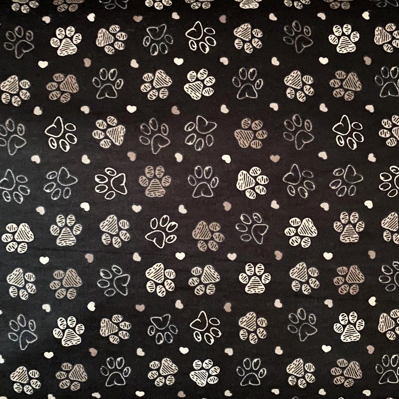 May include: Black fabric featuring a repeating pattern of white and silver paw prints and small white and grey hearts. The paw prints vary in style, some with solid fills and others with striped details.