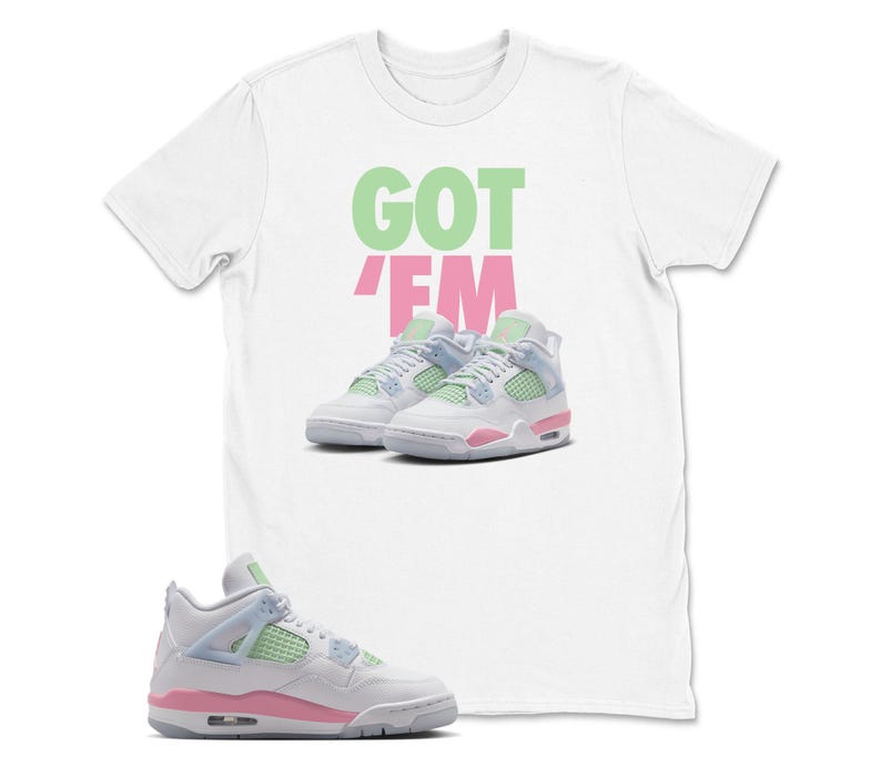 May include: White t-shirt with the text "GOT EM" in green and pink. The shirt features an image of white, pink, and light blue trainers. A single trainer is shown in the foreground.