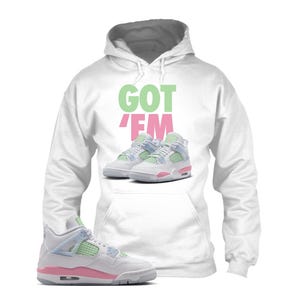 May include: White hoodie with the text "GOT 'EM" in green and pink. The hoodie features an image of trainers in white, pink, and green. A pair of trainers in the same color scheme is in the foreground.