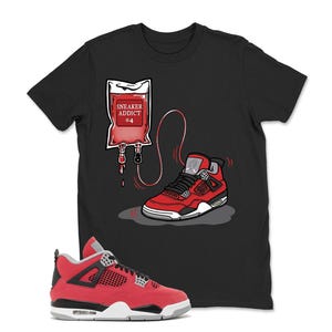 May include: Black t-shirt featuring a graphic of a red sneaker with a matching IV bag labeled "Sneaker Addict 04." The sneaker is red, black, and white. The IV bag is red with white text. The design is a playful take on sneaker culture.