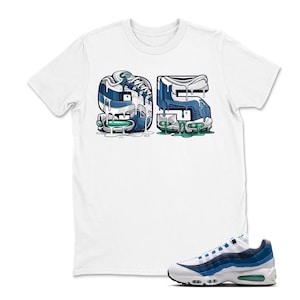 May include: White t-shirt featuring a graphic of the number "95" in a sneaker-inspired design with blue and green accents. A matching white, blue, and green sneaker is displayed below the shirt.