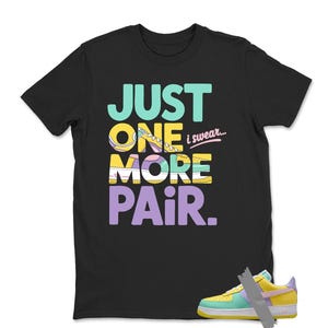 May include: Black t-shirt with the text "JUST ONE MORE PAIR i swear..." in teal, yellow, white, and purple. A colorful sneaker is visible at the bottom right. The shirt is a casual wear item.